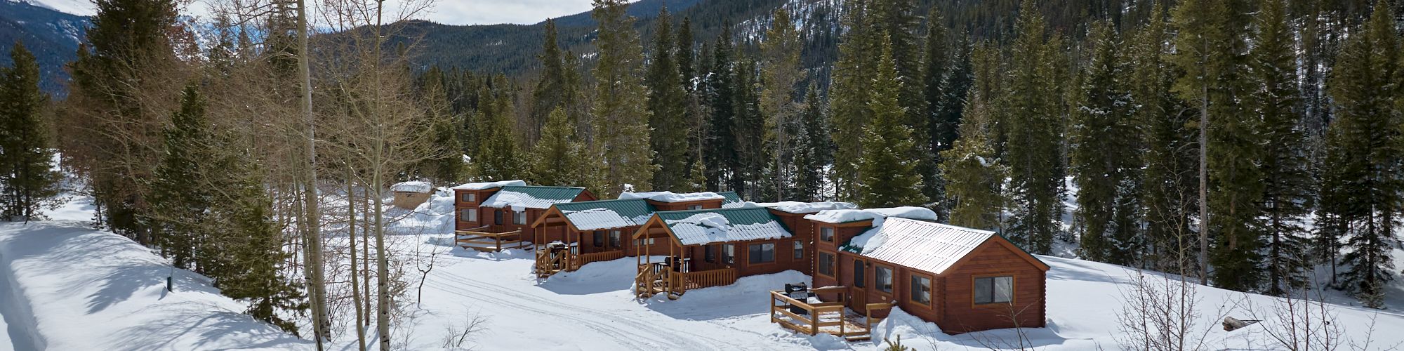 A snowy alpine cabin village nestled among trees and hills, with fresh tracks and blue sky above.